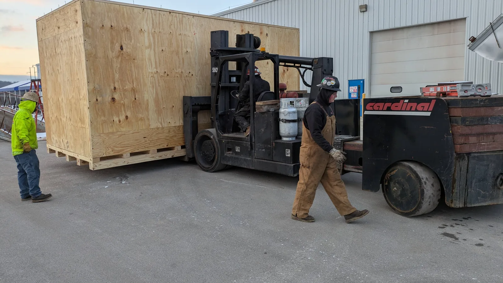 Forklift lifting a large wooden export crate outside a warehouse.