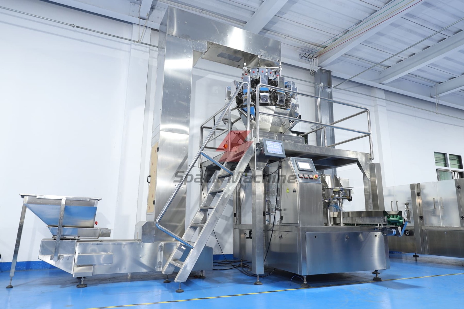 Workshop packaging line with a feed elevator, multihead weigher, platform and rotary pouch machine.